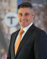 Jeff Gonneville in a dark suit with the T logo behind him