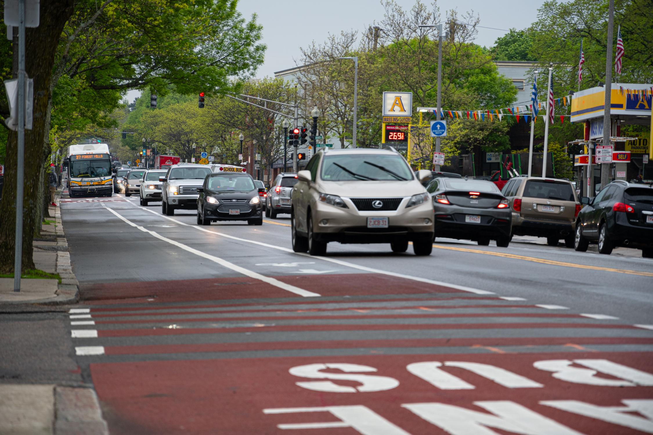 Bus lane, painted red, on Washington Street in Roslindale, with traffic in adjacent lanes and an MBTA bus with a clear lane of its own.