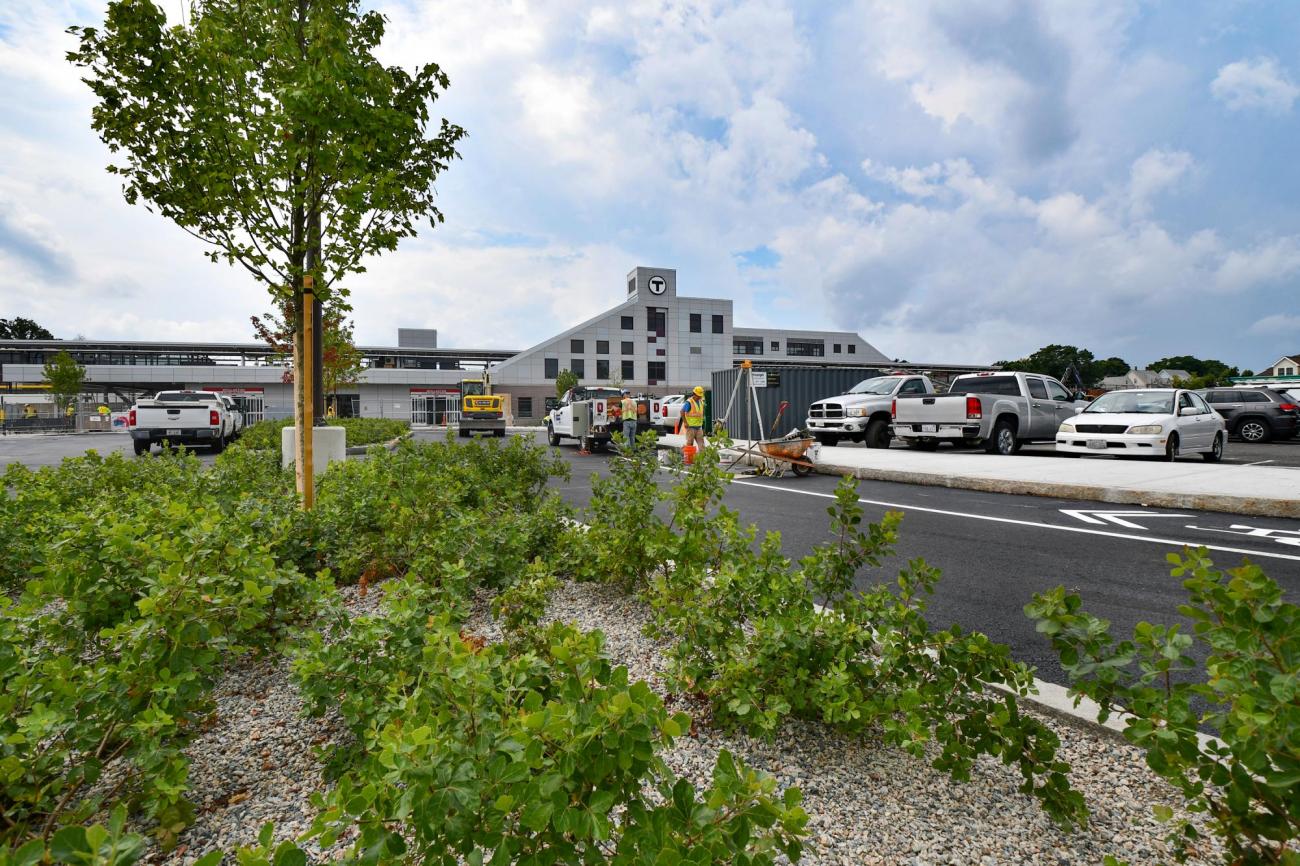 The renovated Wollaston Station viewed from the entrance to the parking lot, with plants in the foreground. (August 7, 2019)