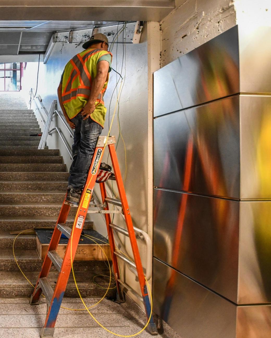 A crewman on a ladder near stairs in Wollaston Station, in the final stages of renovation. (August 7, 2019)