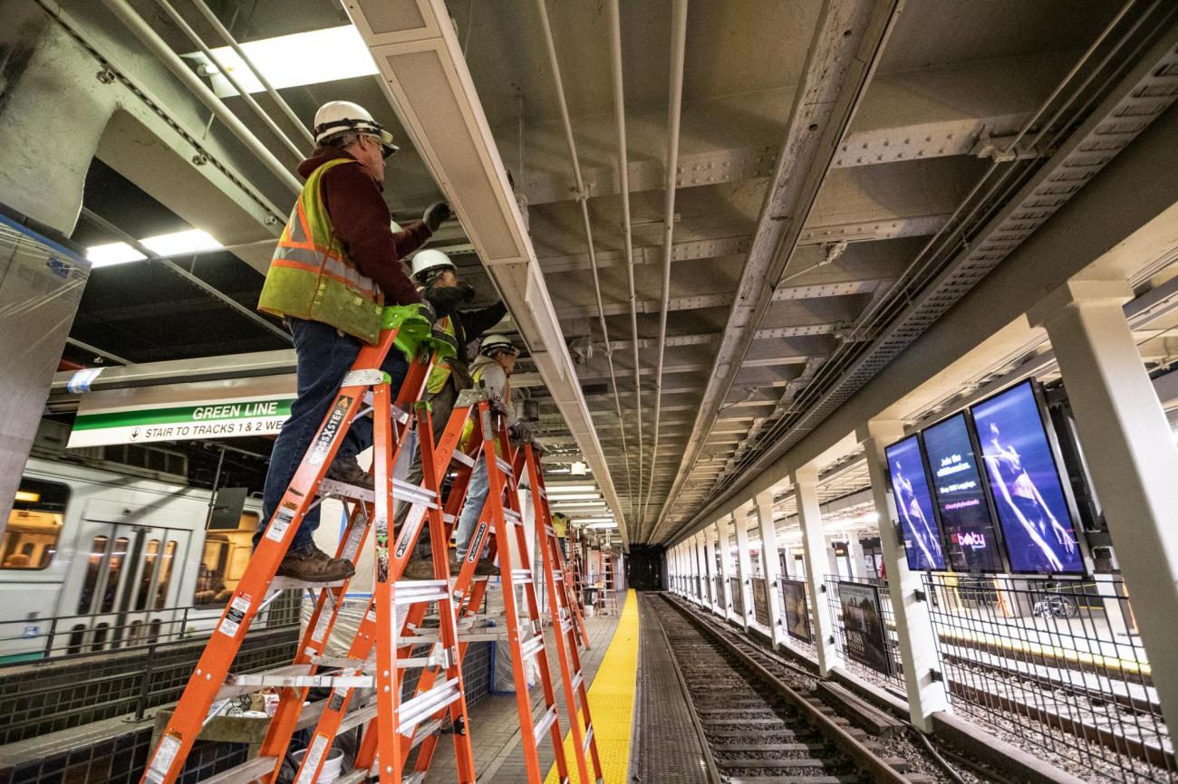 Three crewmen on 3 ladders install new lighting on the Green Line eastbound platform at Park Street.