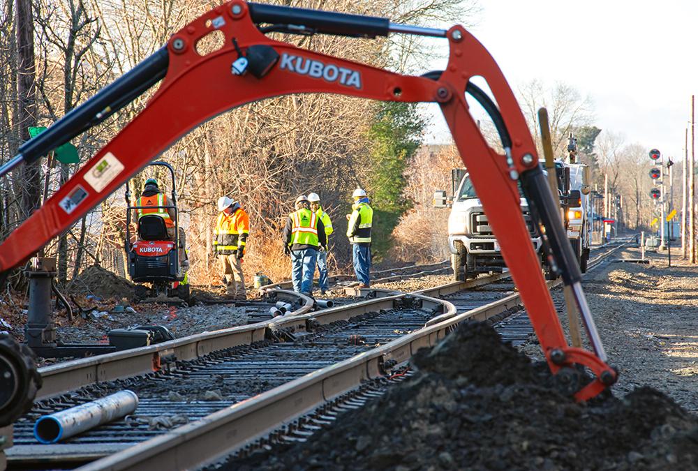 A crew excavates underneath the track to prepare for communication signal line installation near Walpole Station on the Franklin Line of the Commuter Rail (January 2020)