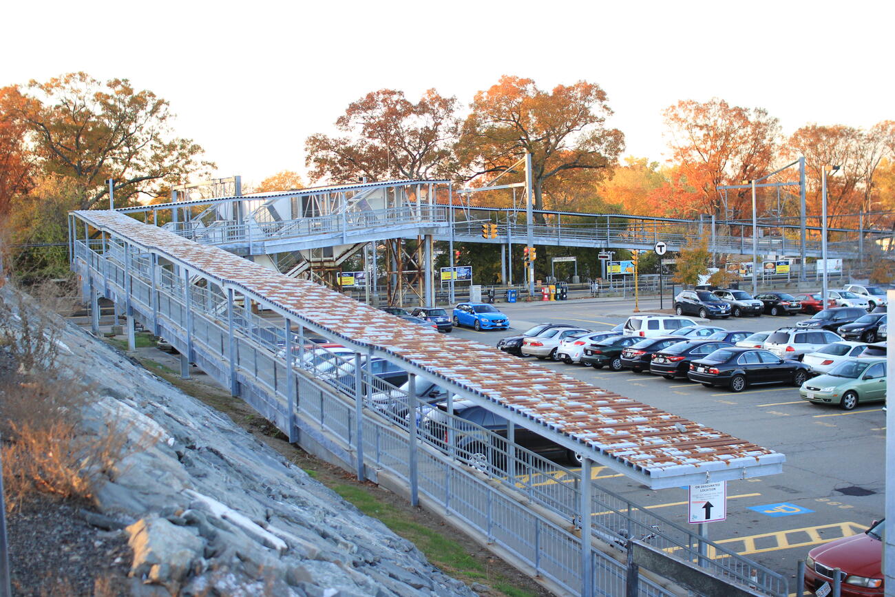 View of the current South Attleboro accessibility ramp prior to reconstruction. The ramp overlooks the semi-full parking lot on an autumn day during sunset. 