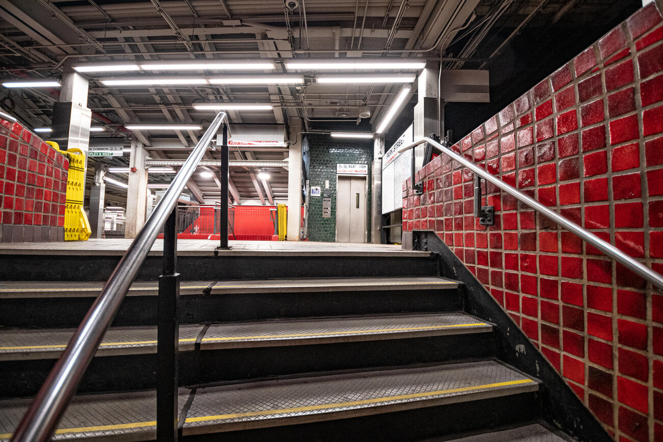 A close-up of stairs inside Park Street Station. An elevator is visible on the opposite wall