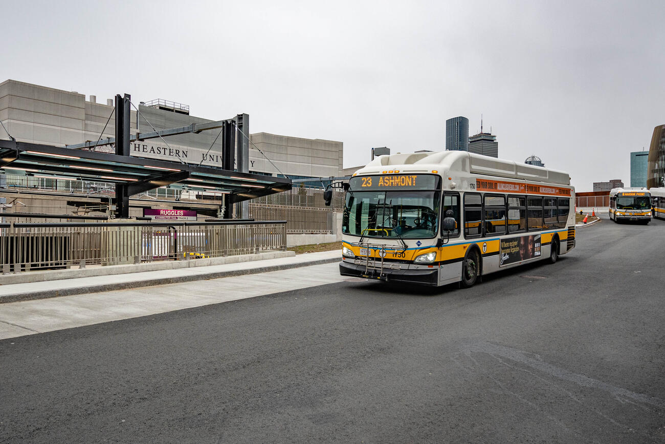A bus approaching a Ruggles busway with signage of Commuter Rail platform in the background