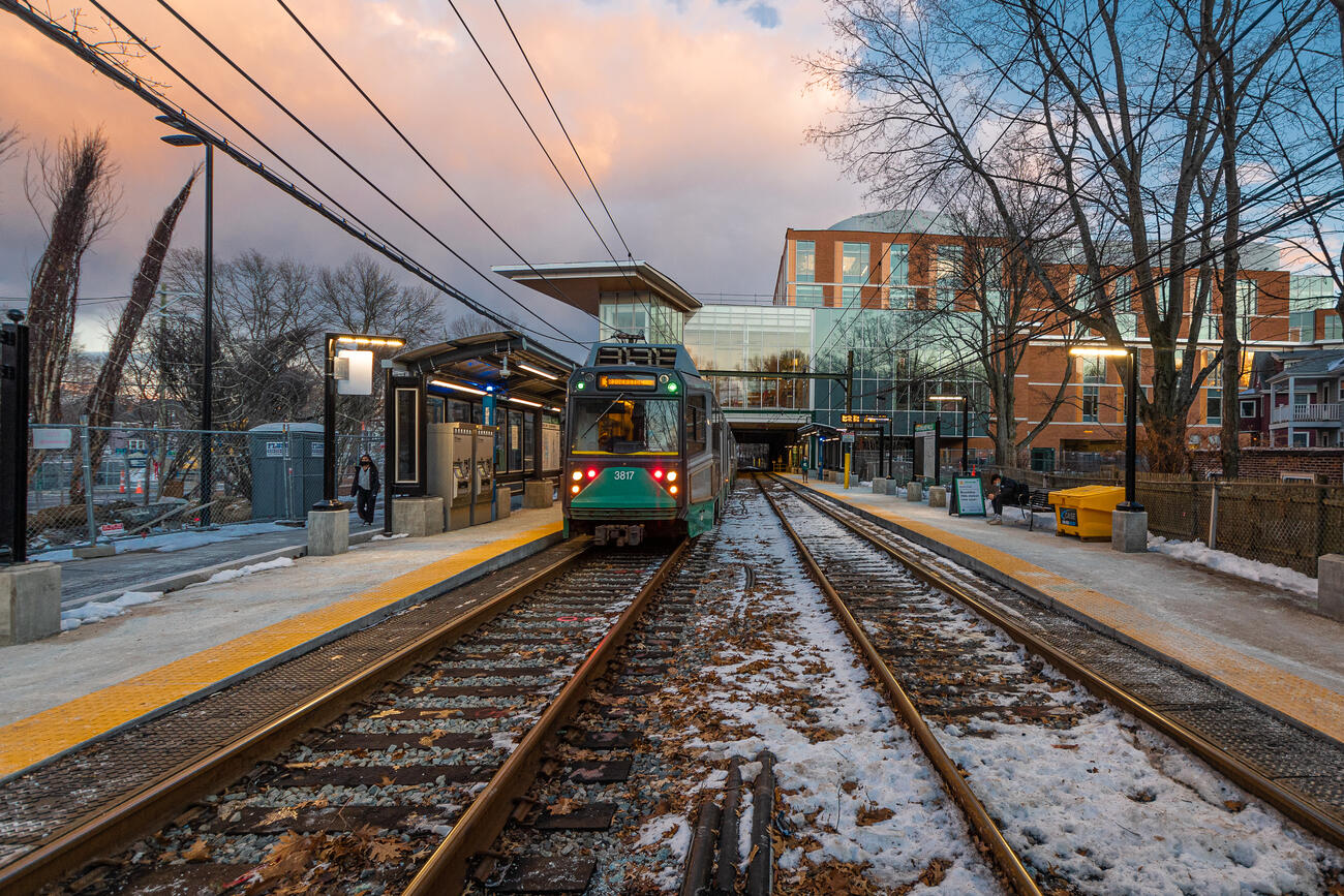 A green line trolley waits on snowy tracks at sunrise