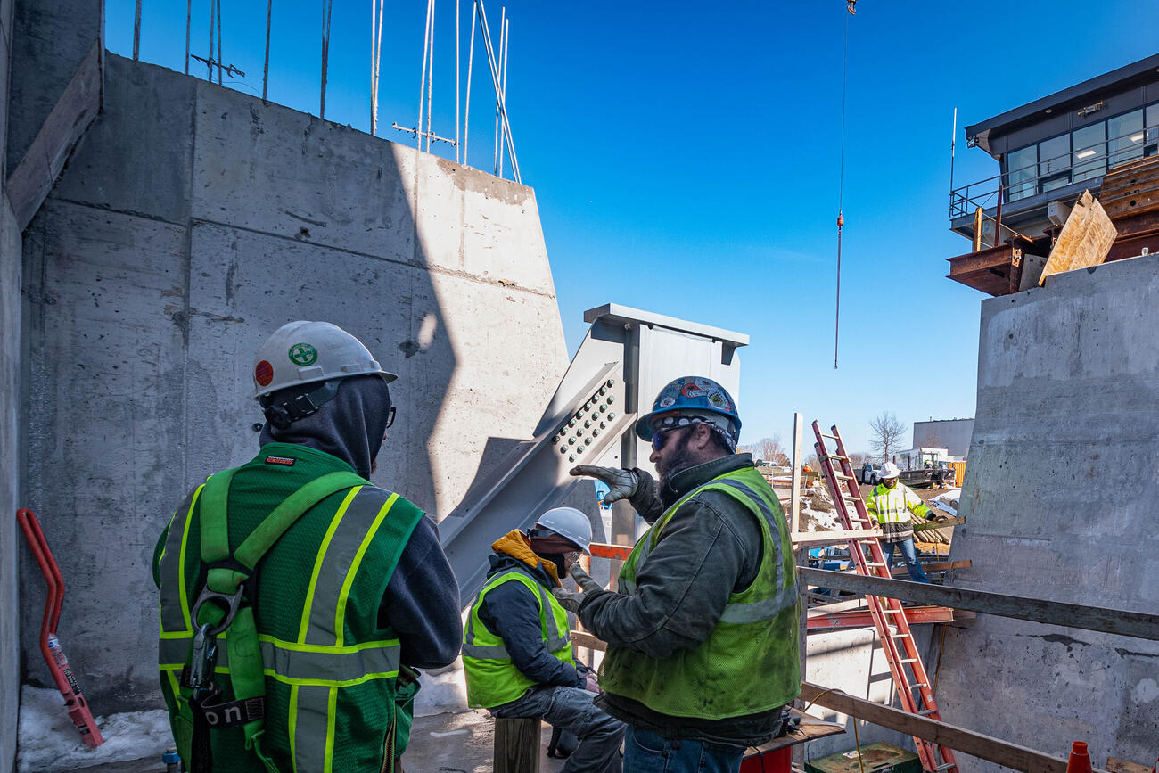 Two crew members in high vis and hard hats discussing something with a third crew member sitting down a few feet away