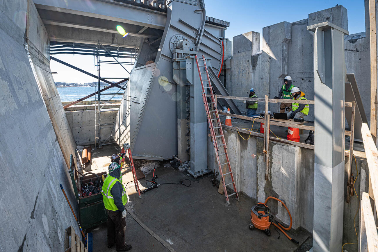three crew members up on a cement platform appear to be talking with two crew members down below