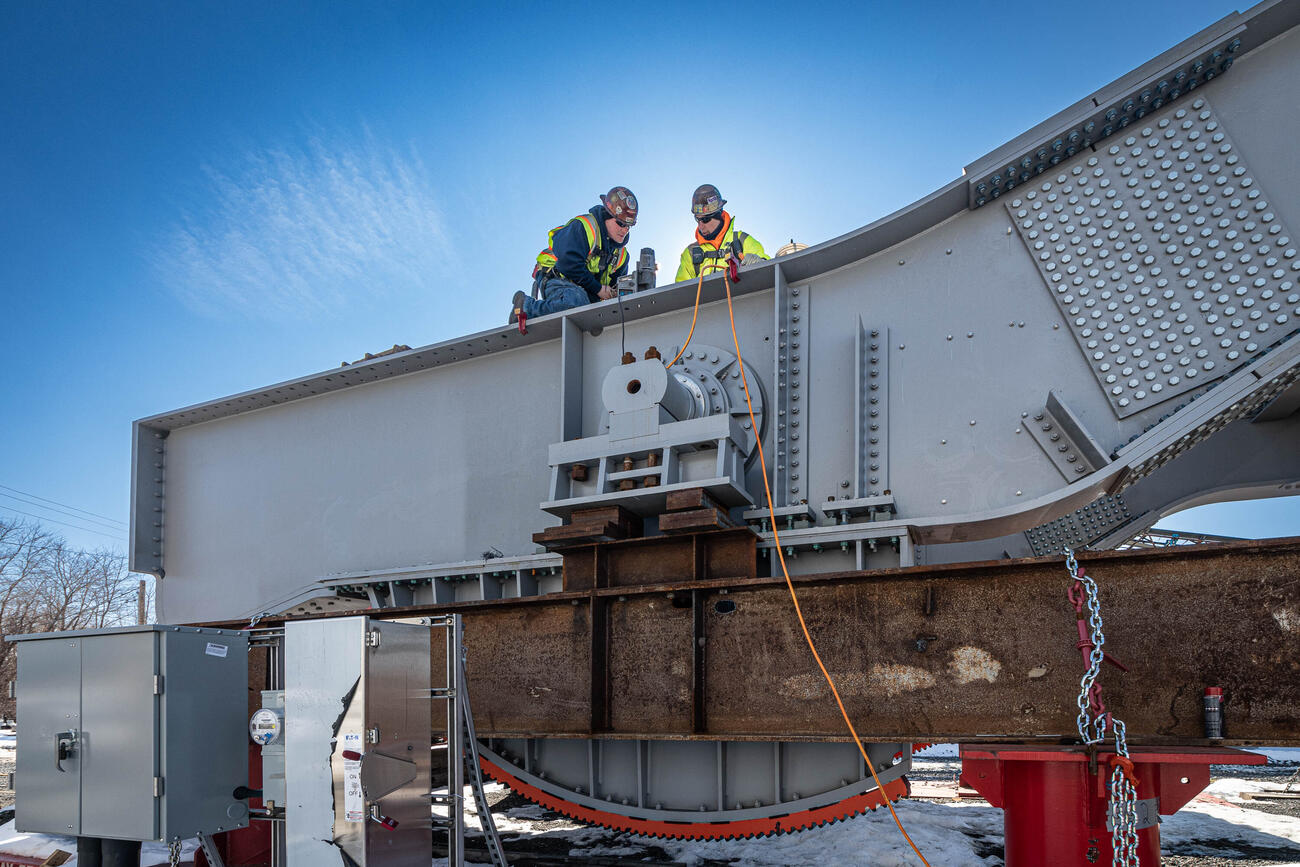 two crew members working on top of a notched moveable piece of the bridge