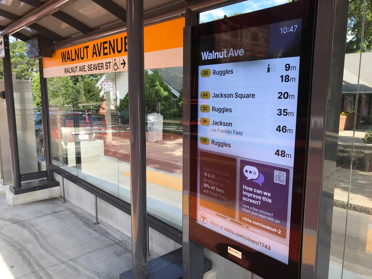 The Walnut Avenue bus shelter on Columbus Avenue has a large digital screen that shows the time, the stop name, and the predicted arrival times for the next six buses scheduled to arrive there. The screen also mentions 50%-off Youth Pass fares, and asks riders to tell us how we can improve this screen by going to this web address: mbta.com/walnut-2