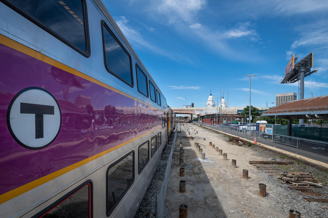 A commuter rail train sits on tracks next to three rows of completed micropiles at Worcester Union Station. The micropiles will serve as part of the foundation for the new, high-level center platform.