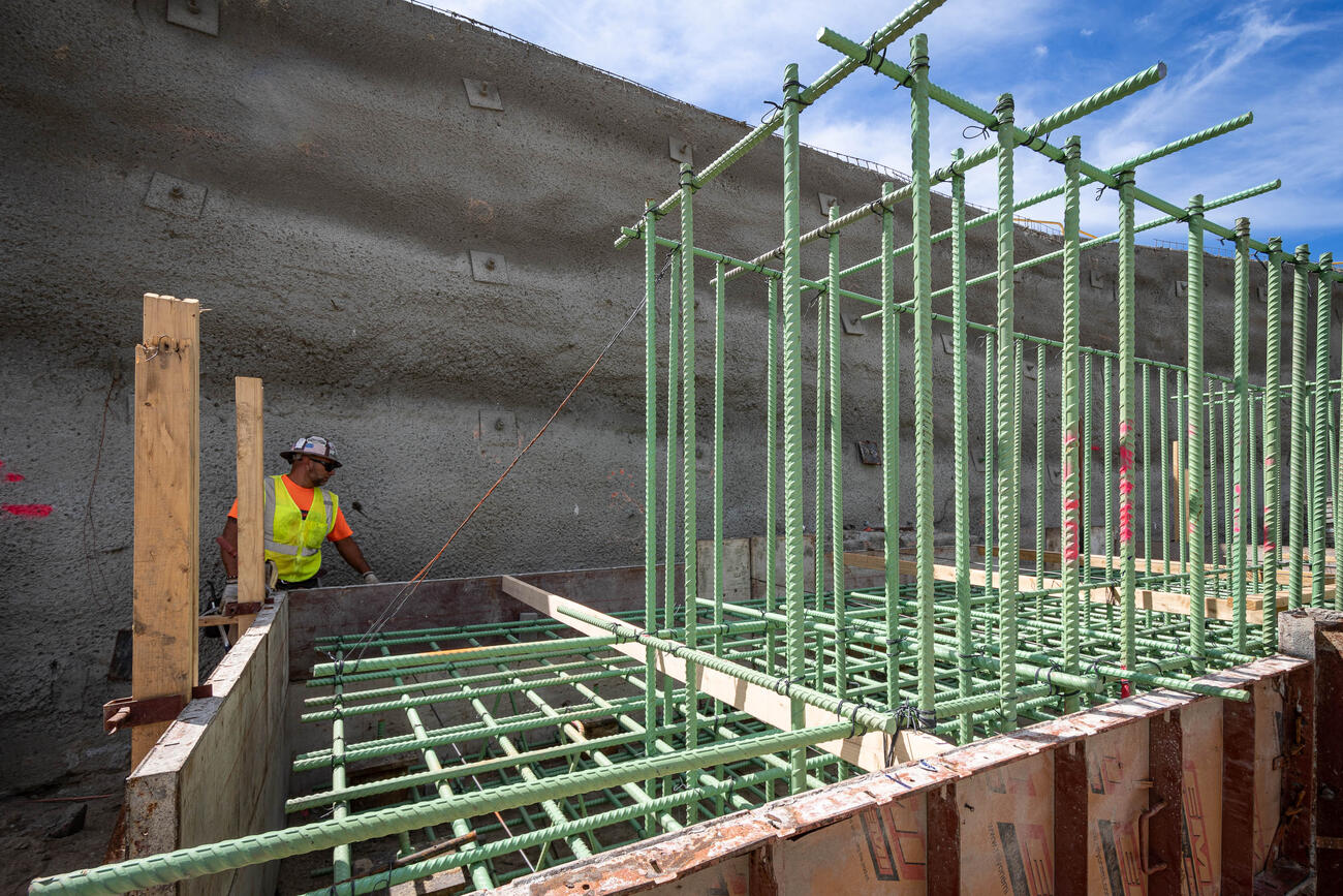 A worker installs steel reinforcement bars vertically and horizontally for pile caps at the north headhouse, pedestrian bridge foundation.