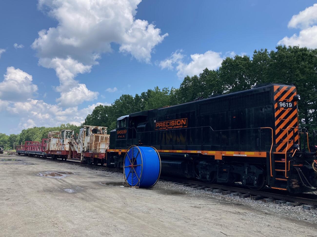 A reel of blue innerduct sits next to a plow train, which will be used to install the innerduct underground.