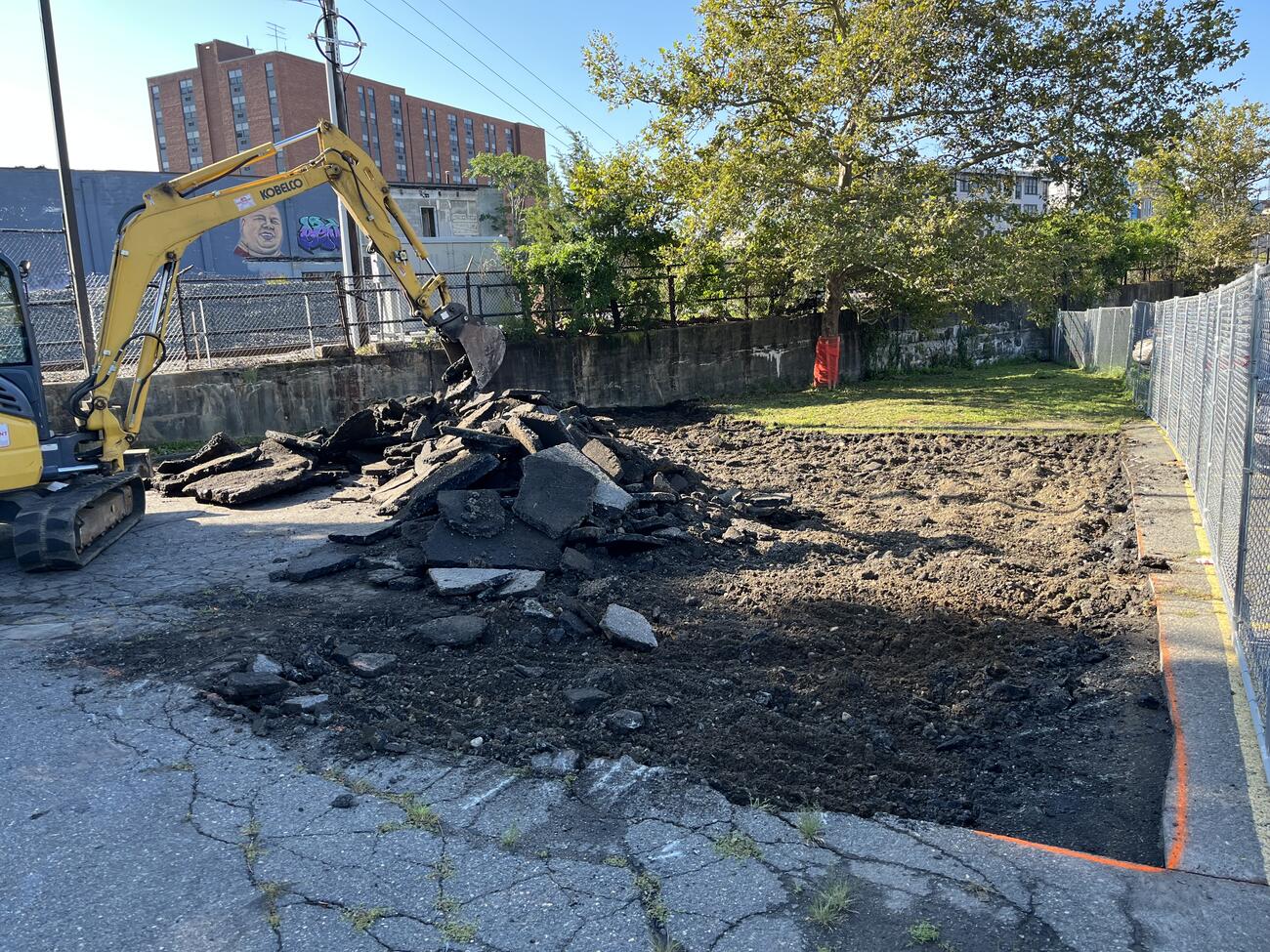 An excavator tearing up asphalt to reveal dirt underneath