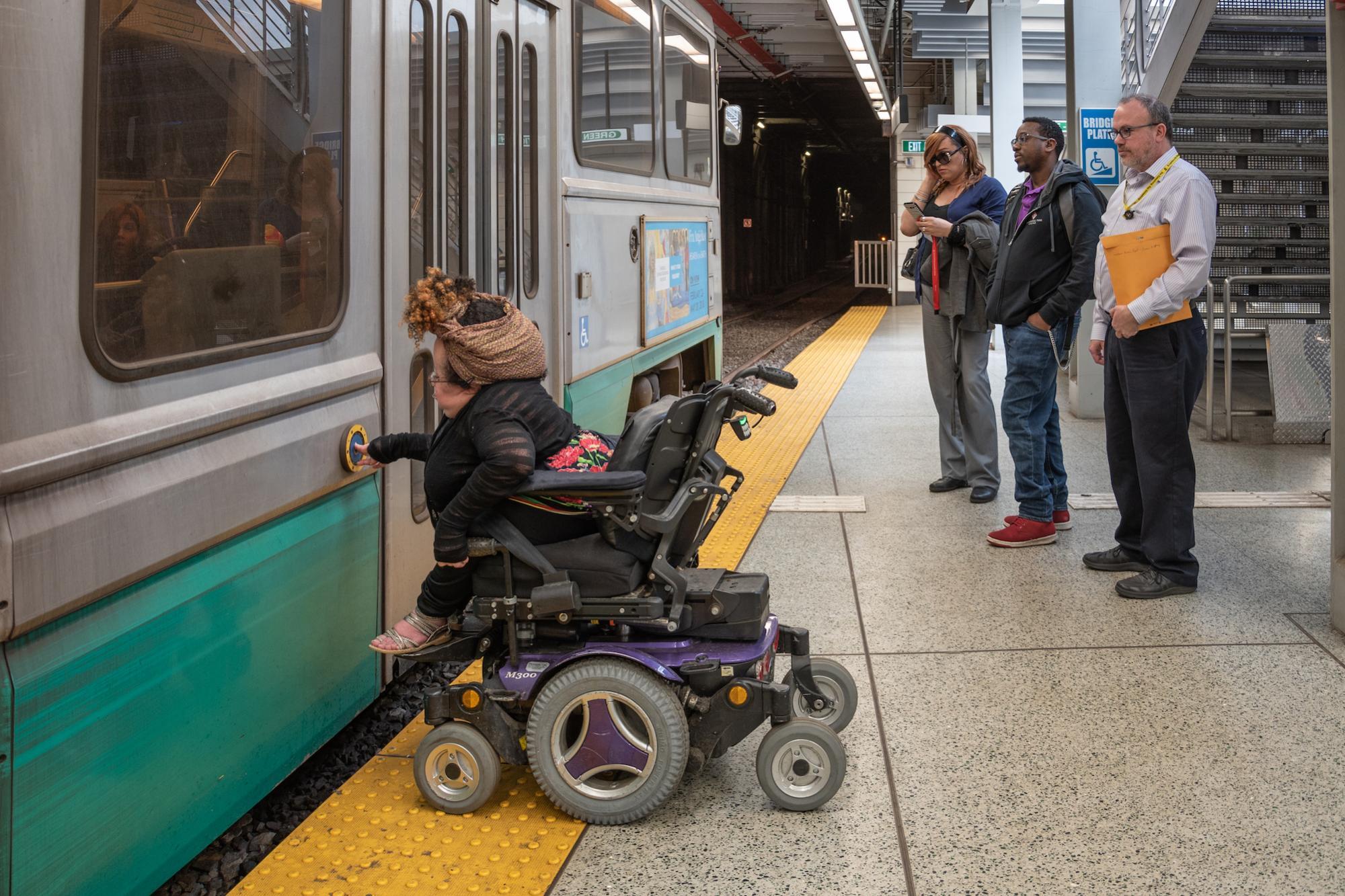 A person in a wheeled mobility device presses the accessibility button on a Green Line train at Government Center Station.