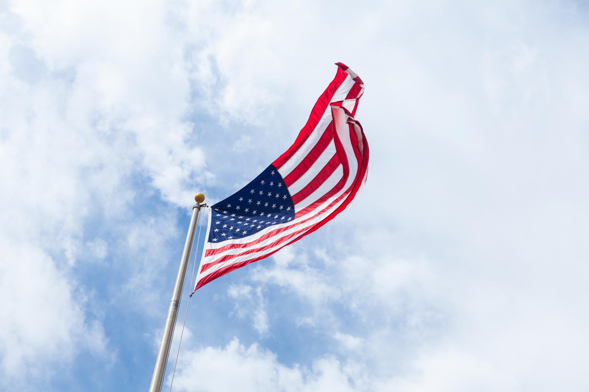 American flag with a blue sky and white clouds in the background. Photo by Brandon Day on Unsplash