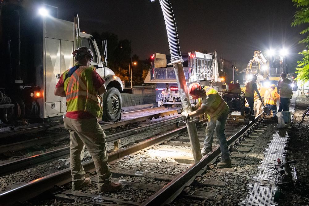 A crew member vacuums up ballast before replacing rail ties on the Orange Line in Medford.