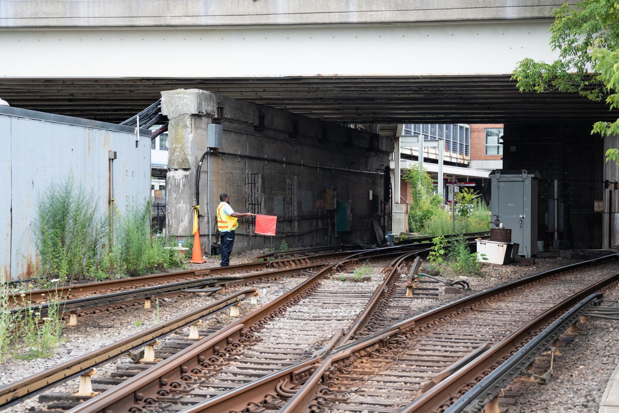 A worker stands near tracks and serves as a human signal, holding a flag to indicate to trains when it's safe to proceed and when they need to stop.