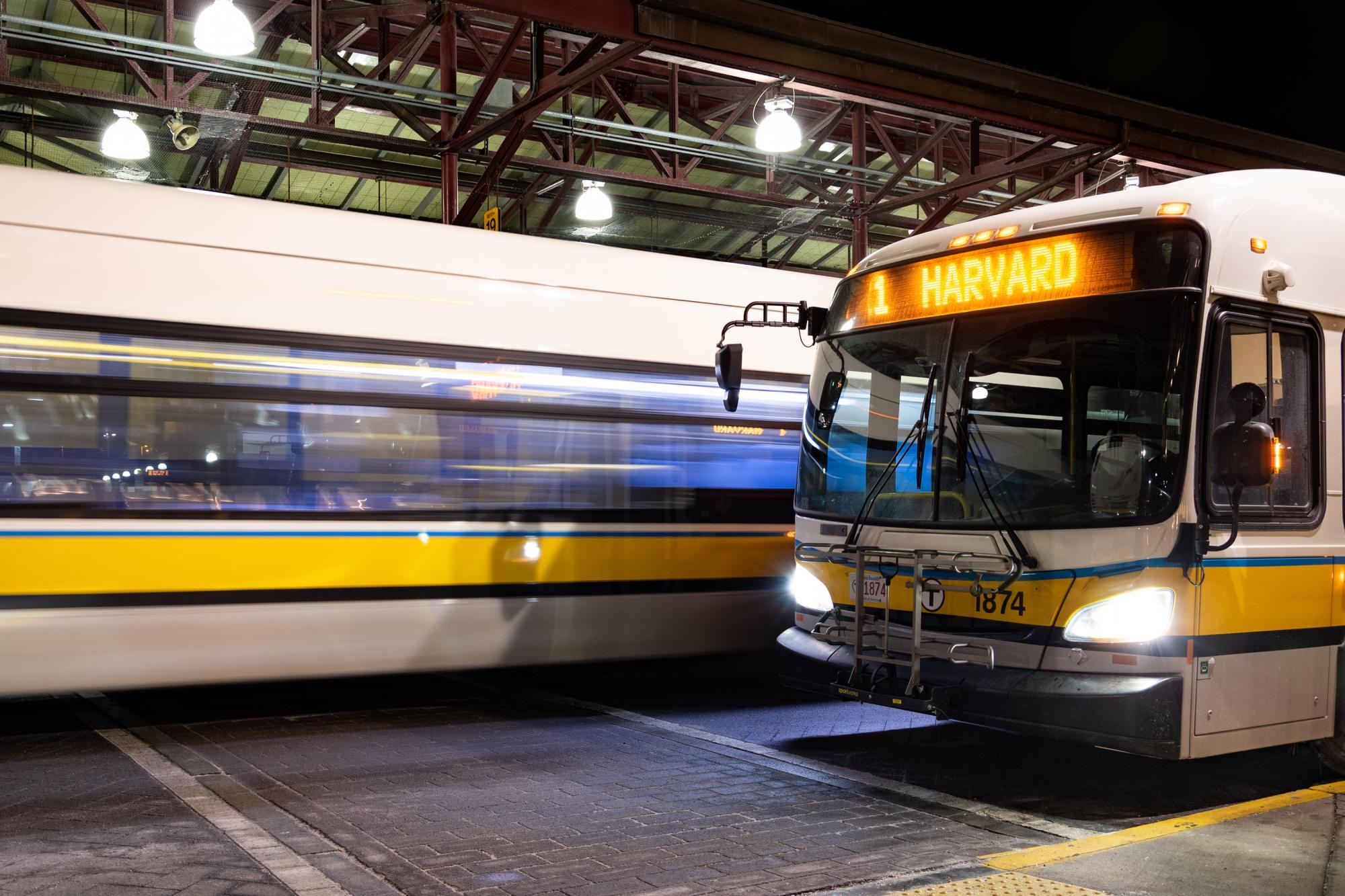 At Nubian Station late at night, a Route 1 bus bound for Harvard waits as another bus zooms by.