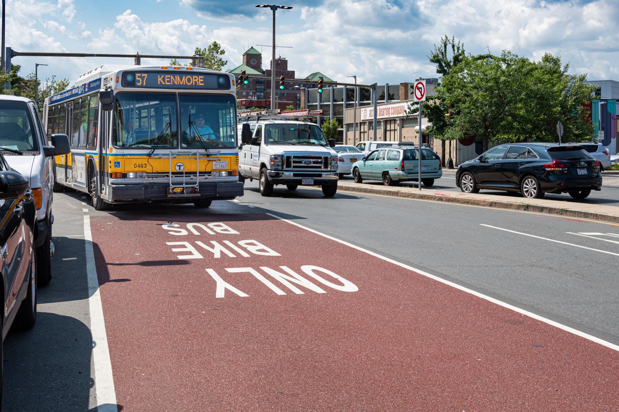 A 57 bus travels in a dedicated bus lane on Brighton Ave in Allston, with "Bus Bike Only" prominently stenciled in the dark red lane.