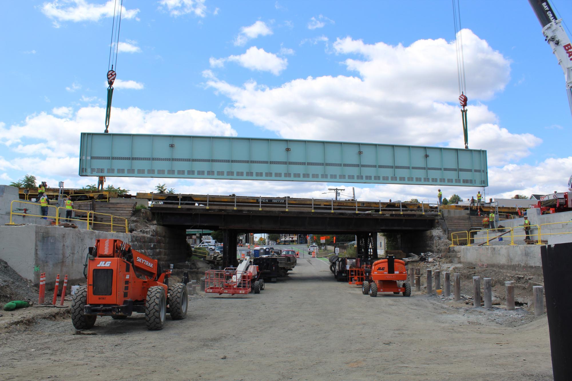 A crane lowers a large, green, steel girder beam into place on the Washington Street Bridge/Underpass in Somerville. They are the first steel bridge girders to be installed as part of GLX.