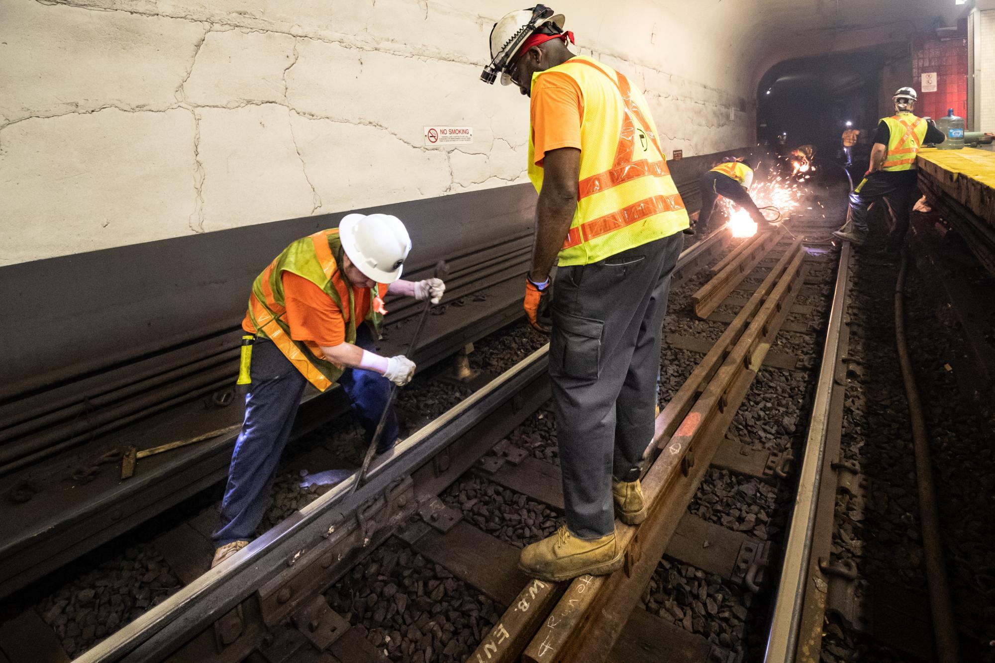 A crew member separates joints of rail, as other workers weld rail in the background, during track replacement work near Bowdoin.