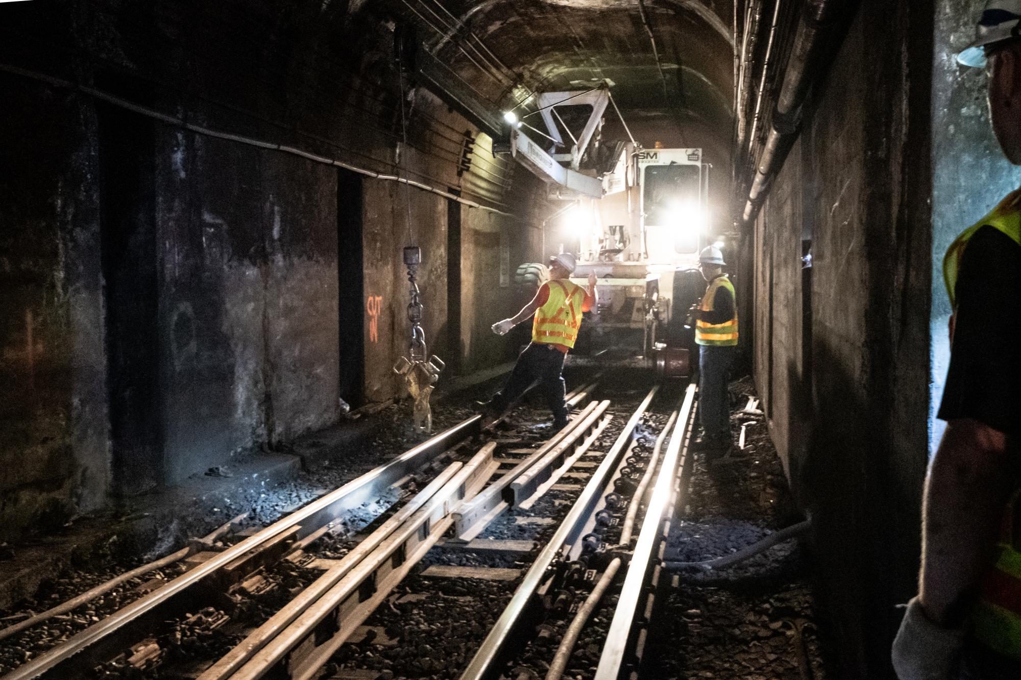A crew works on rail maintenance in a tunnel, between Bowdoin and Government Center, with heavy machinery in the background.