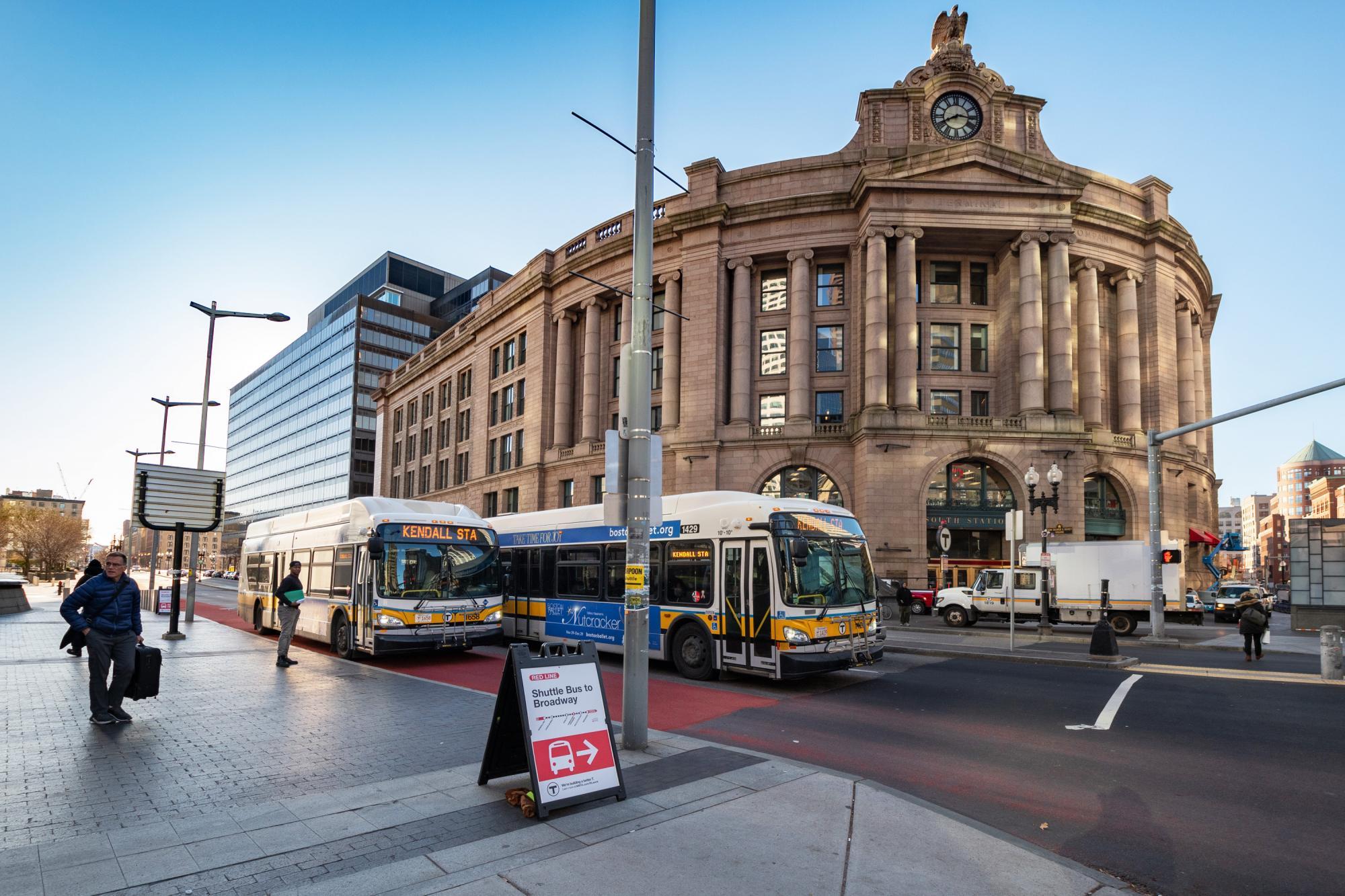 Two bus shuttles (replacing Red Line service), in the bus lane outside South Station, bound for Kendall/MIT. An A-frame sign in the foreground shows where to board the shuttles bound for Broadway.