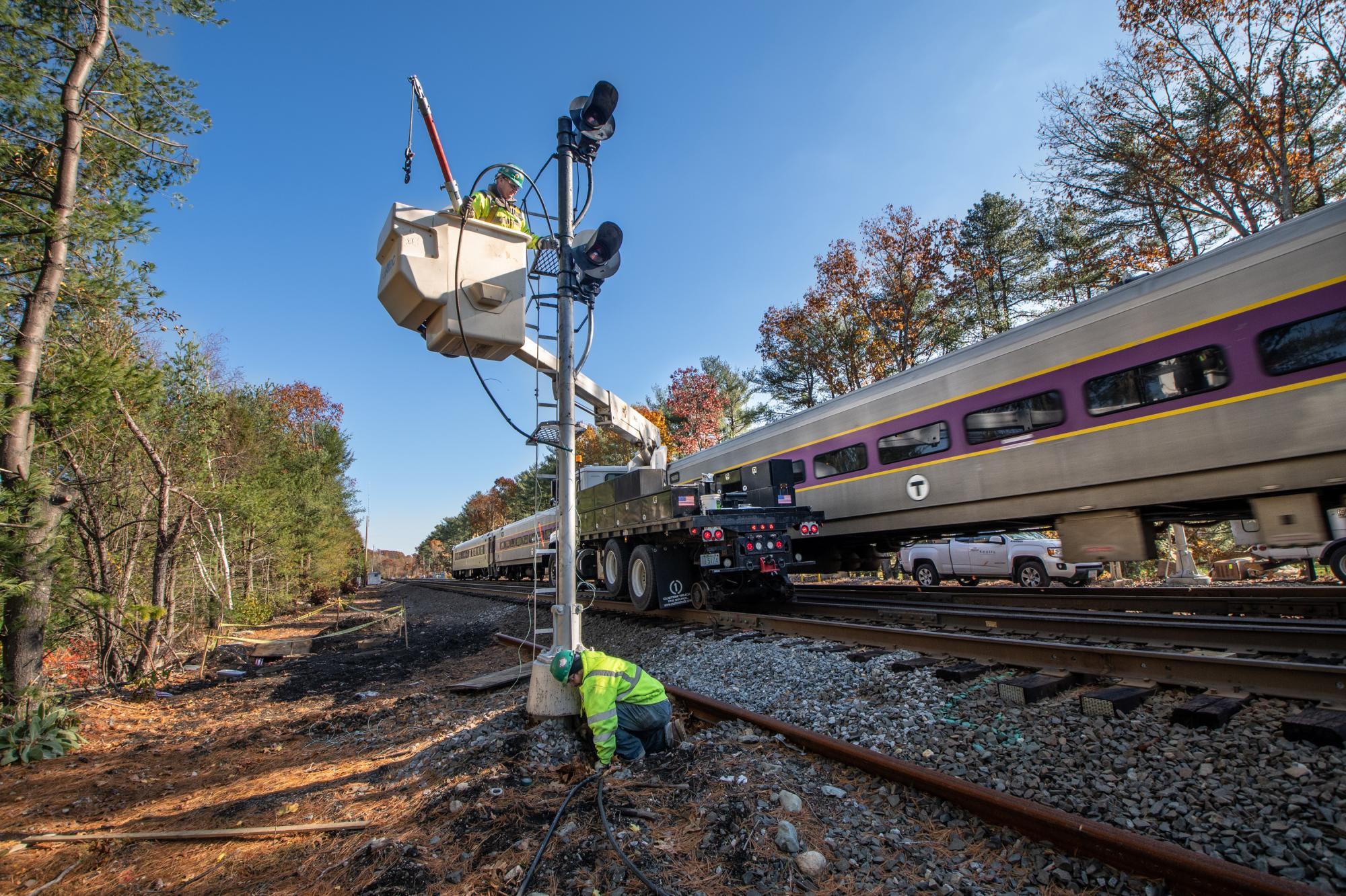A crew works on signal upgrades in Weston as a Commuter Rail train passes by