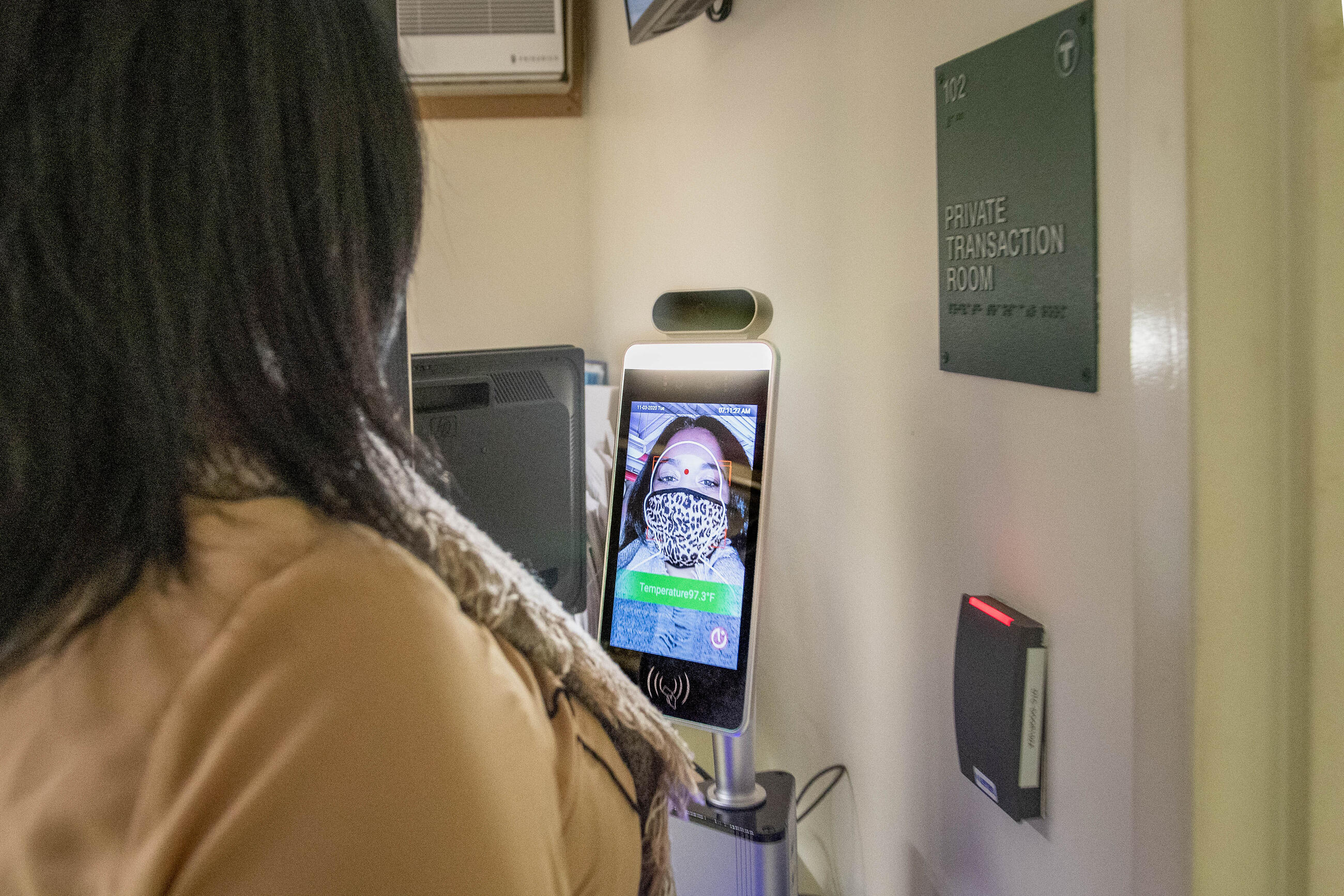 A rider wearing a mask has her temperature taken at a station with a tablet and infared thermometer.
