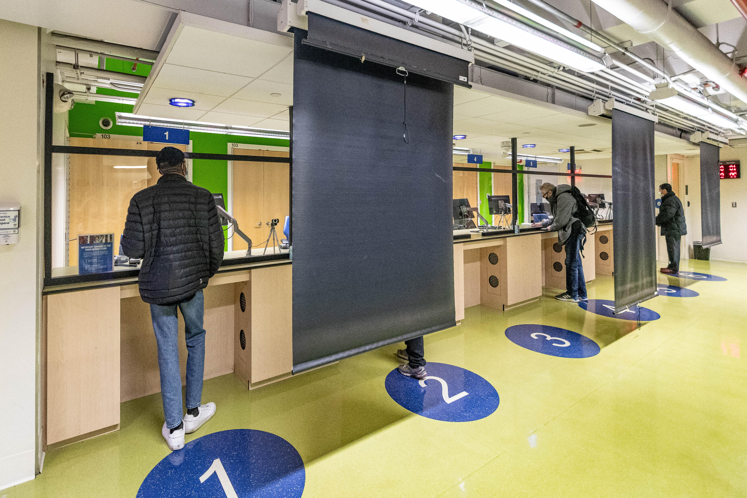 The counters at the CharlieCard Store, labeled 1-6, with some screens drawn down to allow for photos to be taken, and four riders getting service.