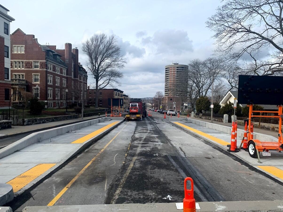 New bus platforms with tactile strips flank Walnut Ave, with heavy machinery in the background.