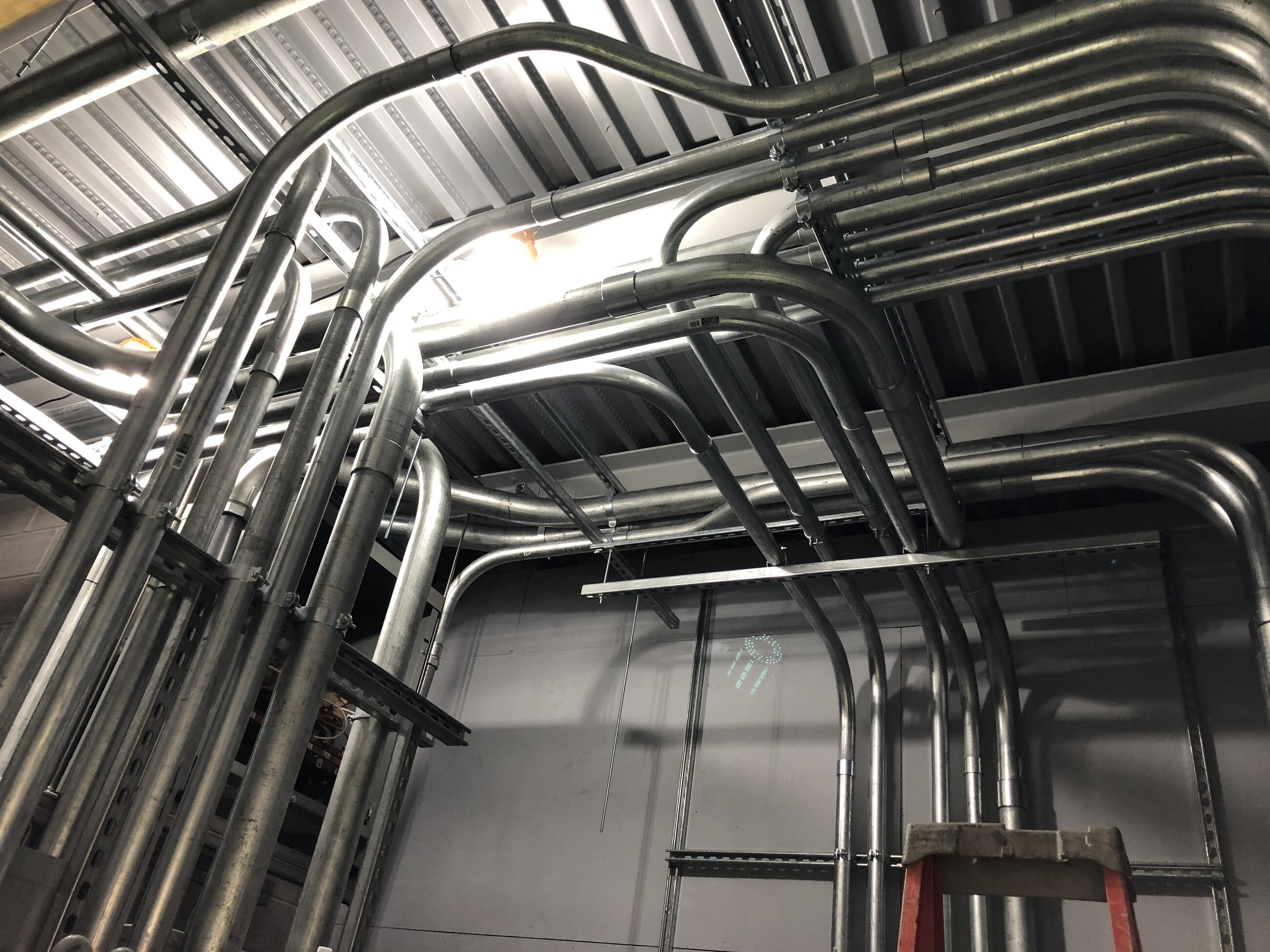 A bundle of steel pipes wrap from the wall to ceiling and back down on the other side