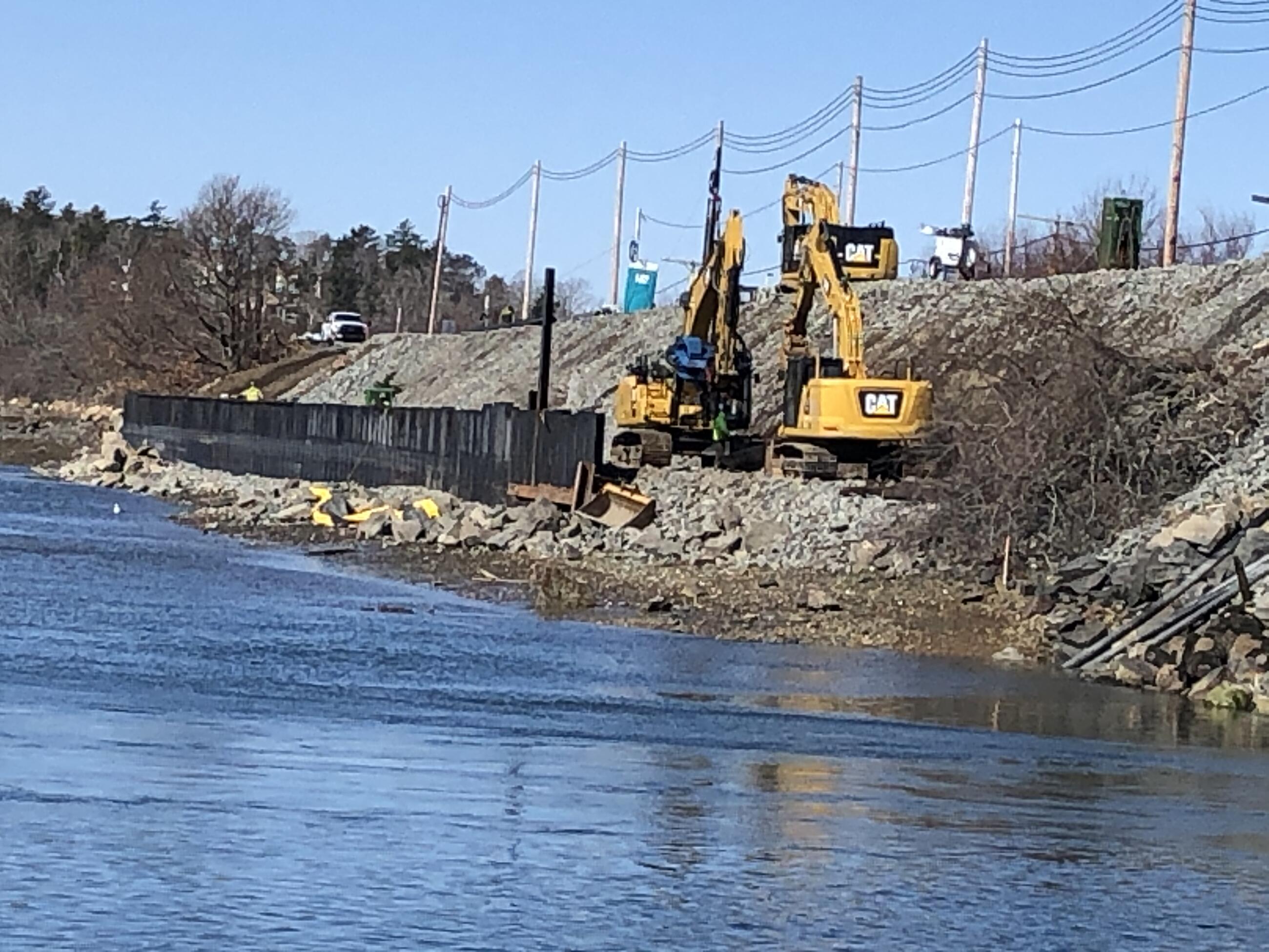 Two yellow excavators working on a pile of gravel on the river shoreline