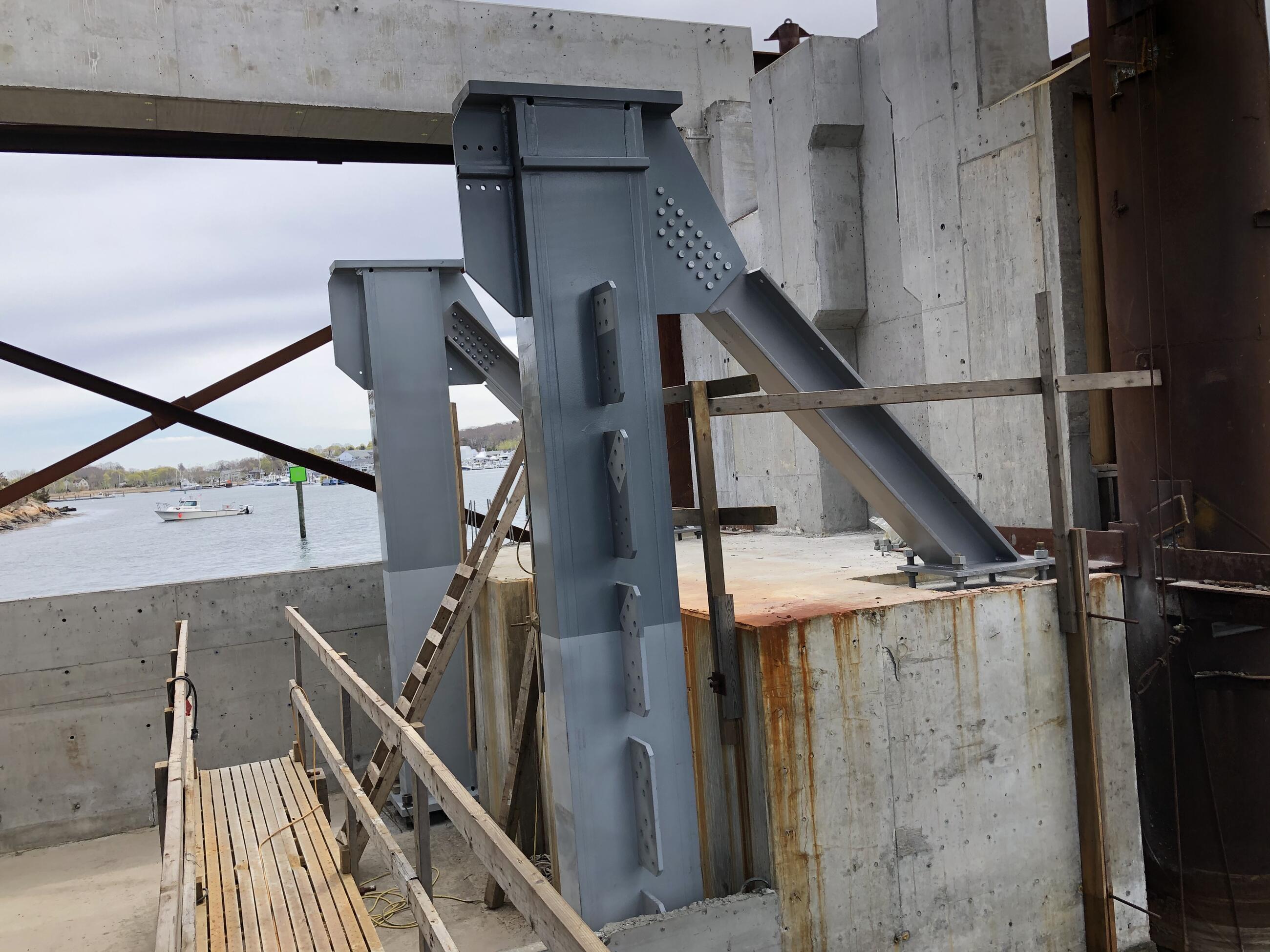 A photo of large grey steel columns that are being installed under a cement base part of the bridge