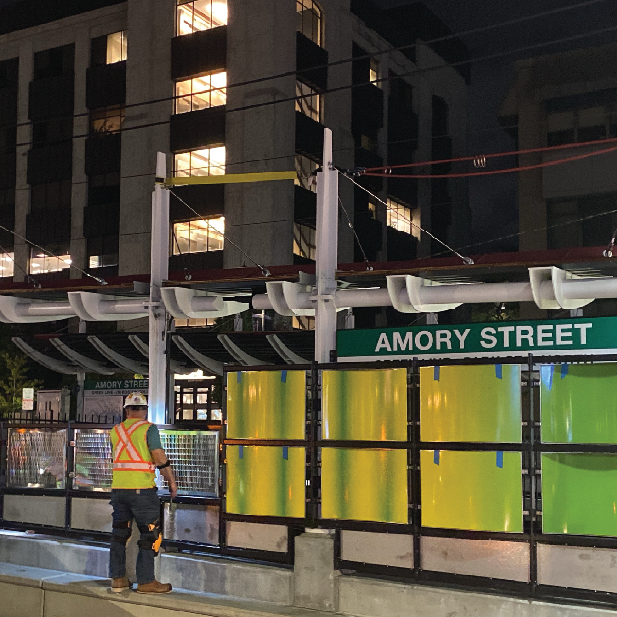 A construction worker in high visibility clothing and a hard hat stands facing the new Amory Street platform at night