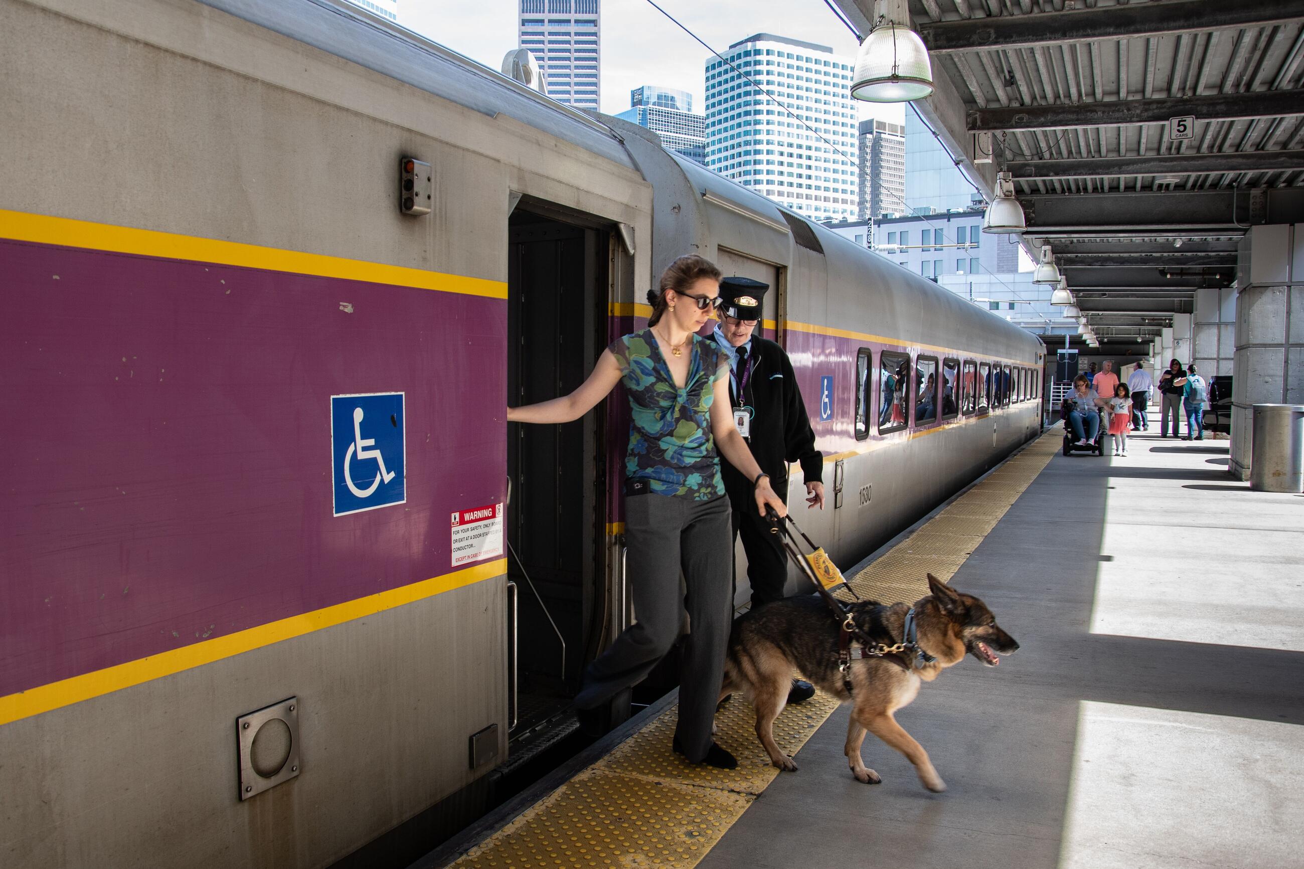 A rider, accompanied by a guide dog, exits a commuter rail train onto a South Station platform