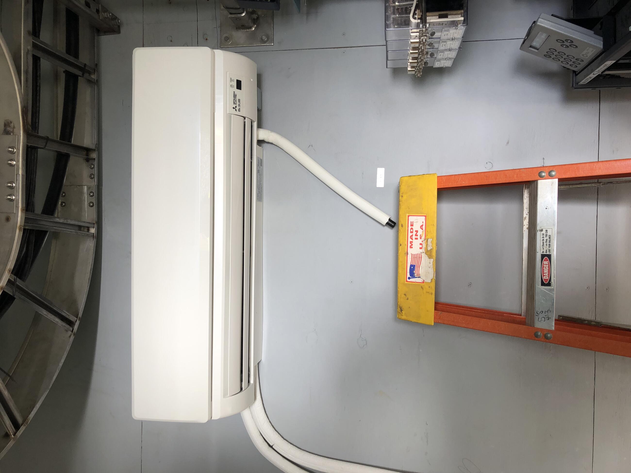 A ductless minisplit heater/cooler is shown attached to a wall of the control tower with a stepladder below it. 