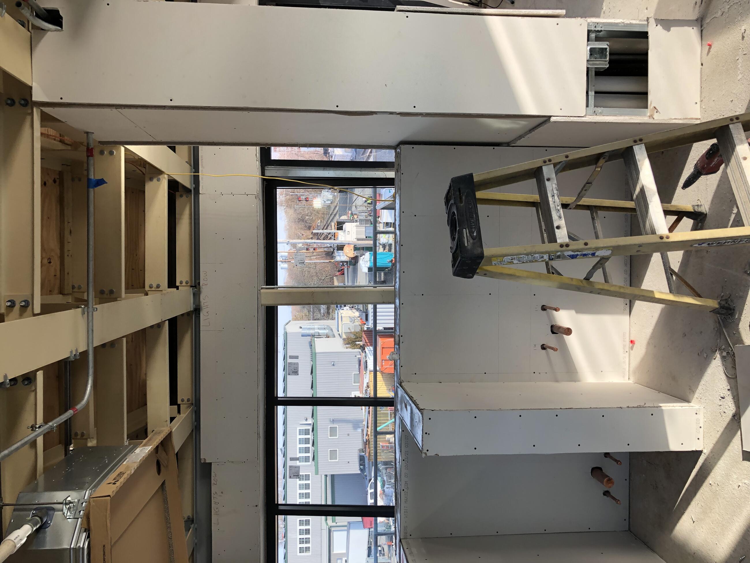 A view of the interior of the control tower facing toward the windows shows that drywall has been installed on walls and to create bays within the room. The ceiling has no drywall and is open so that rafters and beams are visible. 