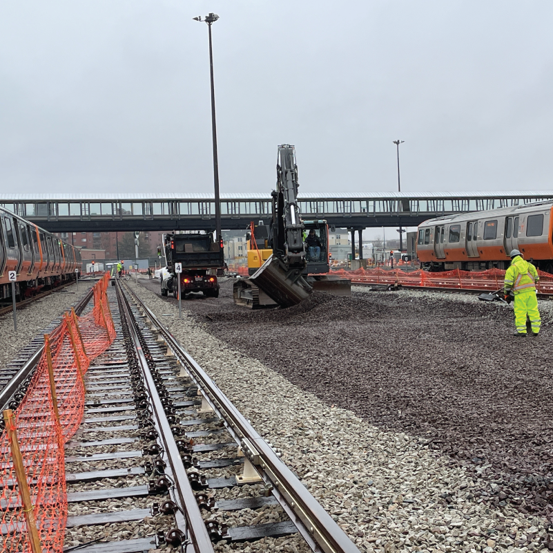 Crew members in high visibility suits spread ballast (rock fill) next to tracks at Wellington Yard