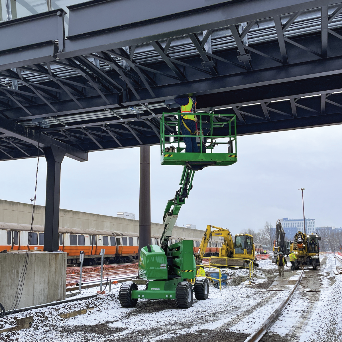 A crew member in a lift installing rail from under a bridge on a snowy day