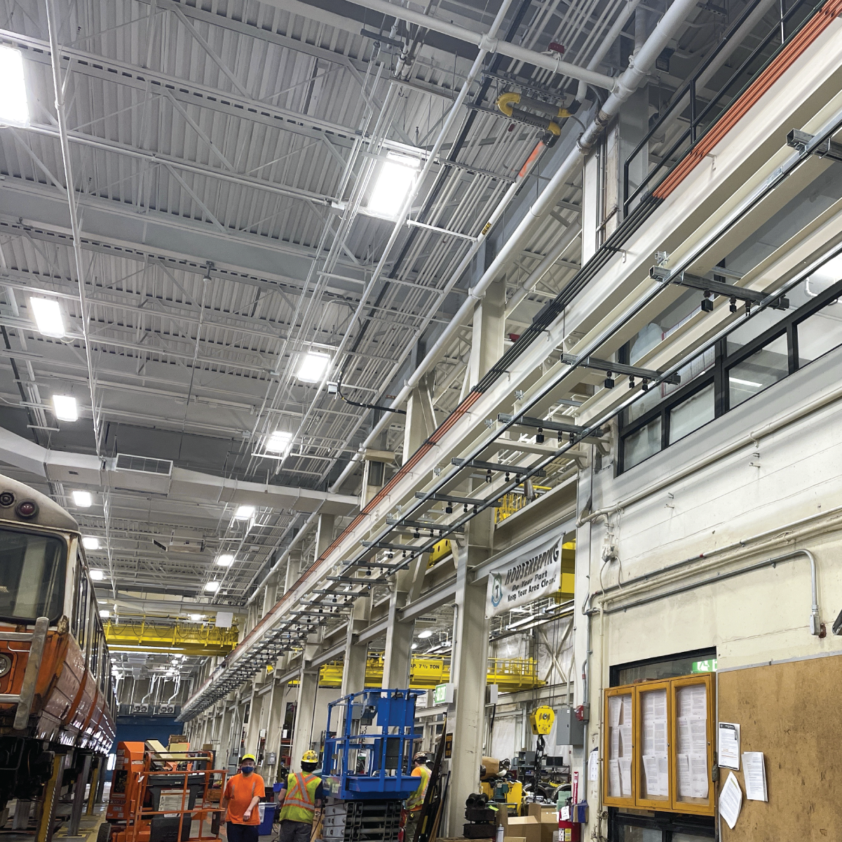 An Orange Line train on a hoist inside the brightly lit Wellington Vehicle Maintenance Facility