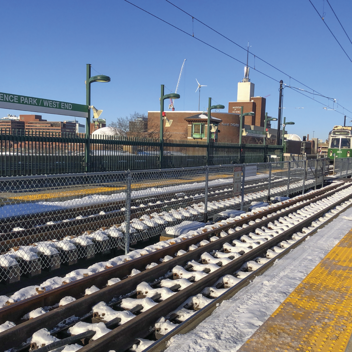 a green line trolley approaching on snowy tracks in front of Science Park/West End Station