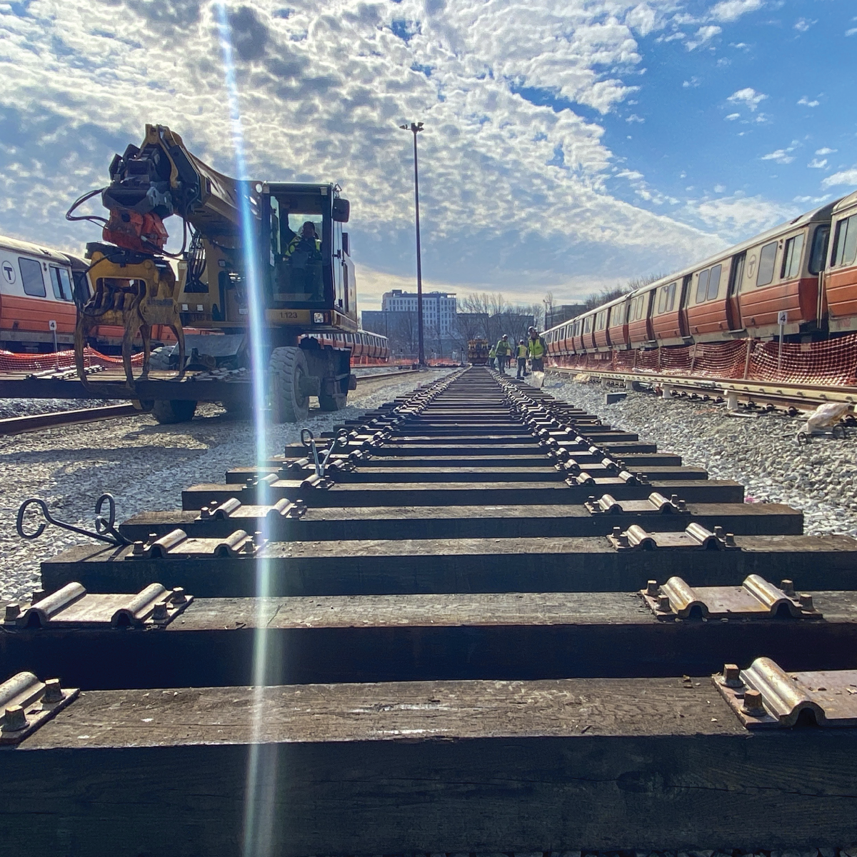 crews working on train tracks with orange line trains parked on tracks on either side