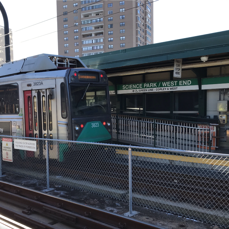 a green line test train behind a chain link fence divider at Science Park station