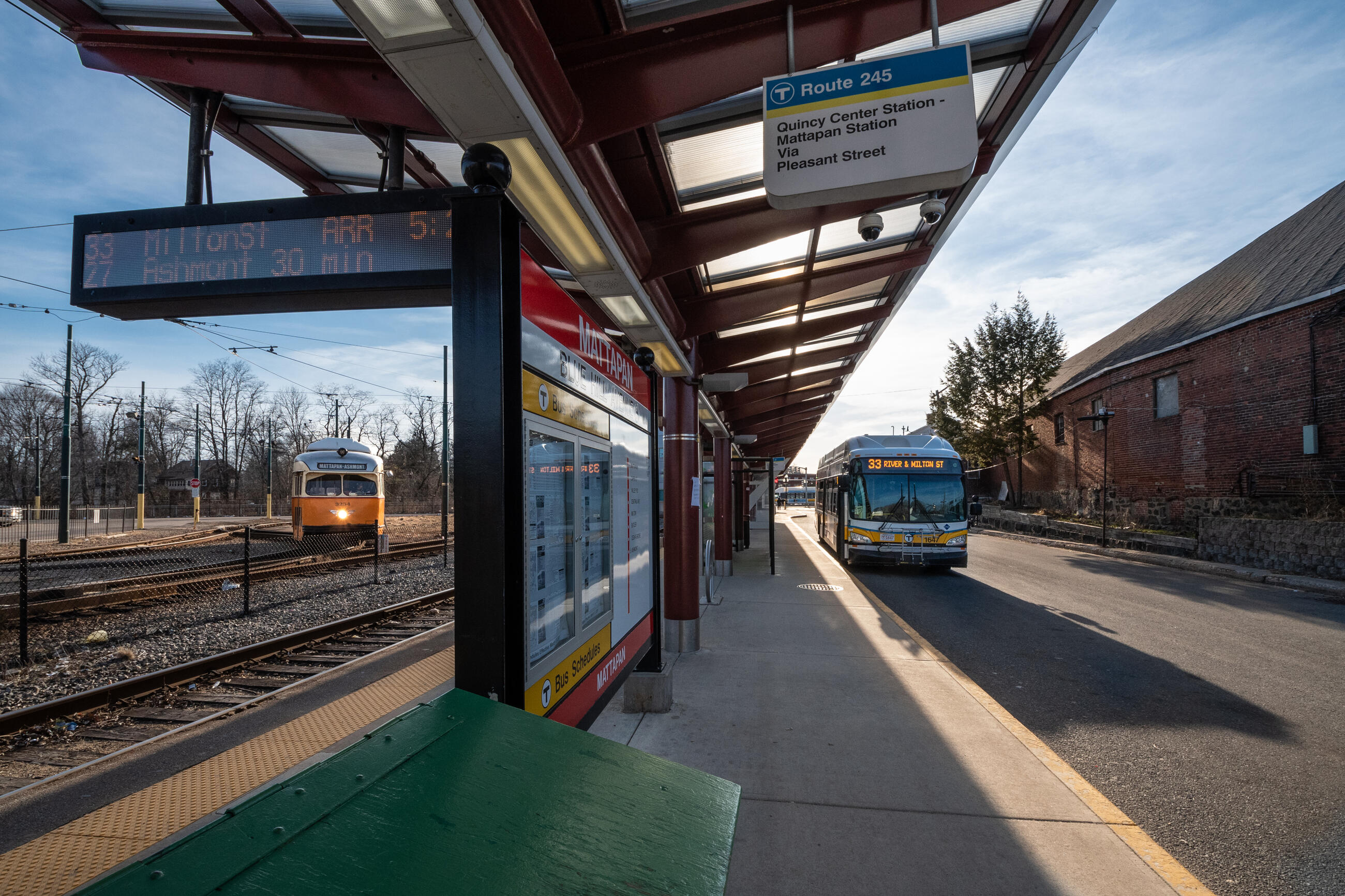 a mattapan trolley to the left of Mattapan station platform and a bus to the right of the platform, both appear to be arriving at the same time