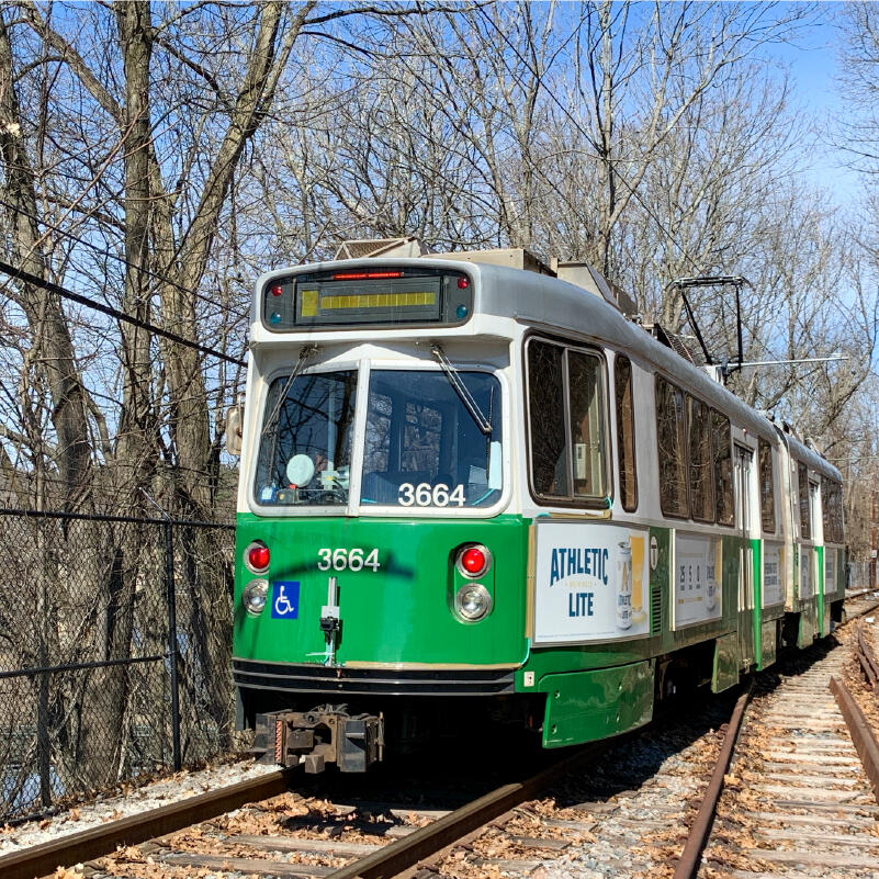 a close up of a green line train on tracks in front of bare trees and a blue sky