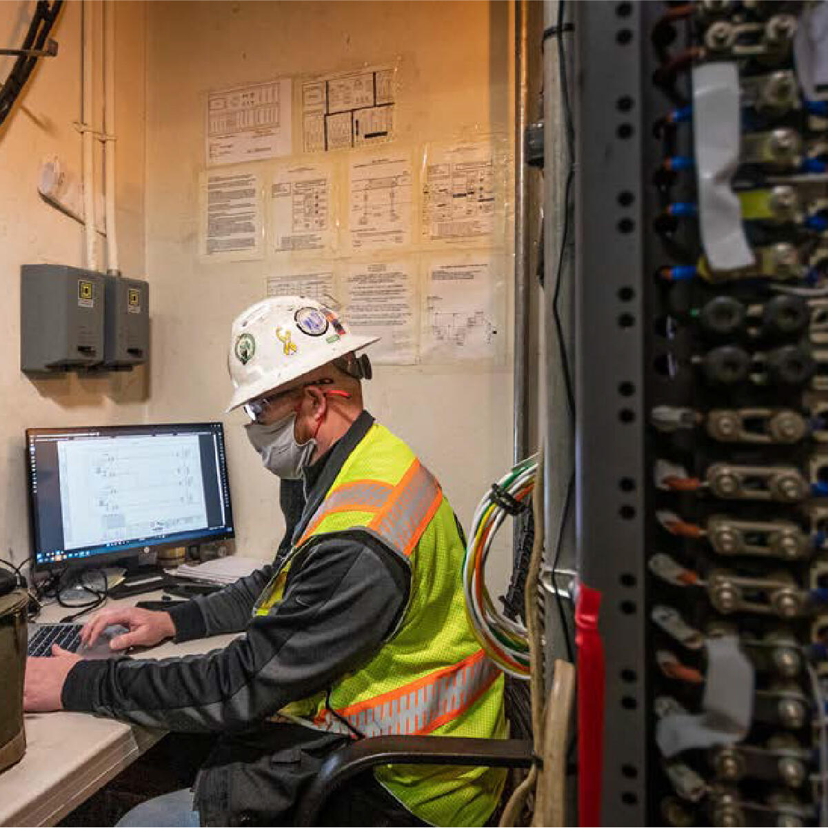 a worker in a high visibility vest and hard hat sits using a computer at a desk