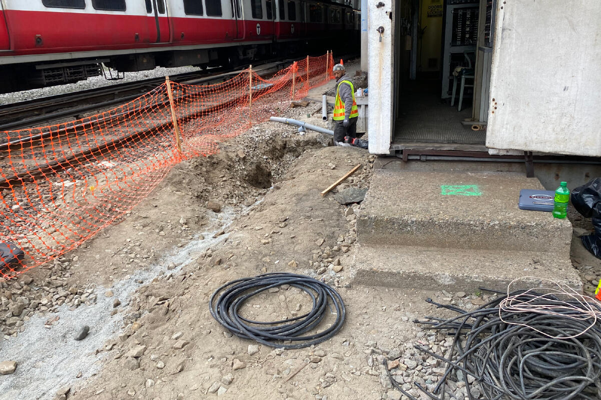 a construction crew members stands in a dirt ditch outside next to a red line train on tracks