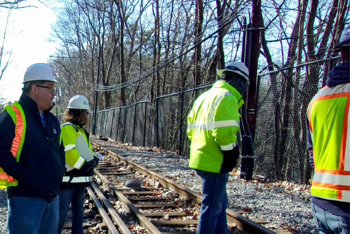 four people in reflective vests and hard hats stand by train tracks